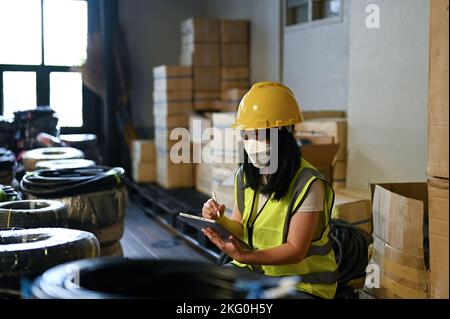 Professional young Asian female warehouse worker or female QC engineer working in warehouse, checking an inventory, using tablet. Stock Photo