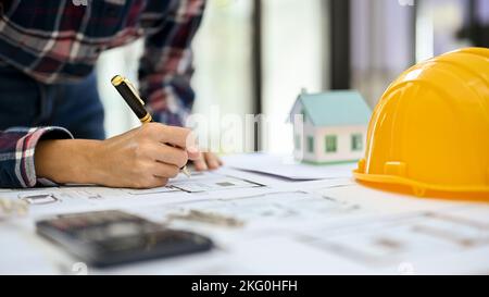 Professional Asian female engineer or architect taking notes on paper, working and checking on the blueprint in the office. cropped shot Stock Photo