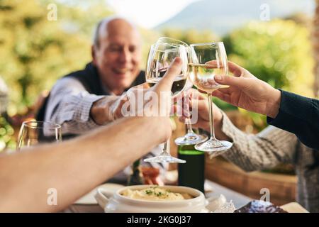 Friends, wine and toast on a patio with happy, cheerful and people celebrating and sharing a meal outdoors. Family, hands and cheers in celebration of Stock Photo