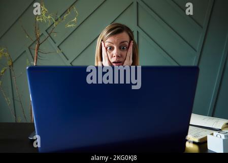 Shocked woman looking at laptop screen with rounding eyes. Excited emotional reaction at online news Stock Photo