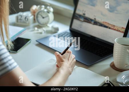 Freelancer working at home office. Woman using laptop and writing in notepad sitting at table in home office Stock Photo