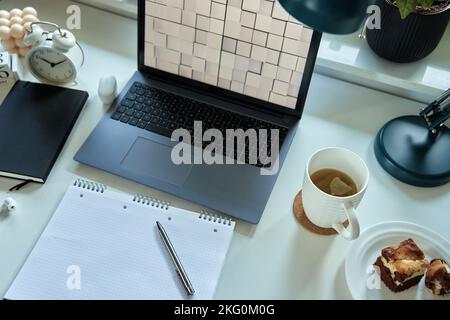 Home office workplace with laptop, documents and cup of tea placed on table in front of window. Remote work concept Stock Photo