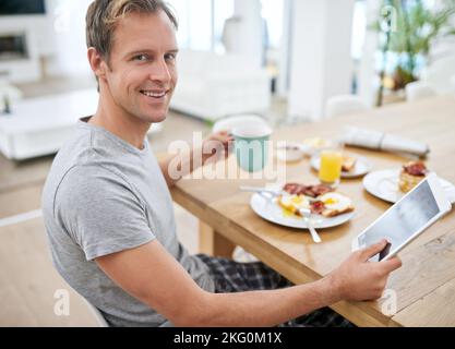The pleasures of a Saturday morning. Portrait of a handsome man using his tablet while having breakfast at home. Stock Photo