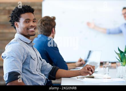Feeling confident about my career potential. Handsome African professional smiling confidently while a presentation is being given in a modern Stock Photo