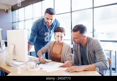 Putting their heads together. three coworkers going through paperwork together. Stock Photo