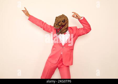 Crazy young guy wearing pink suit and funny dinosaur mask dancing and having fun at party Stock Photo