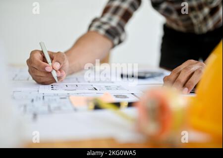 close-up image, A professional Asian male engineer holding pen, working on a blueprint, checking scale, planning building process. Stock Photo