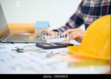 Professional Asian female architect or engineer using scientific calculator and laptop computer, working in her office. cropped shot Stock Photo