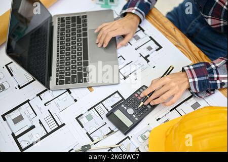 Top view, A professional female architect or engineer working at her desk, using scientific calculator and laptop computer, planning building process. Stock Photo