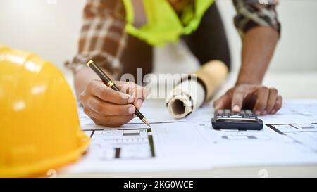 cropped image, Professional Asian male engineer or construction engineer writing something on blueprint, using scientific calculator, working in the o Stock Photo