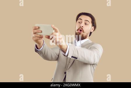Funny businessman taking selfie pleasantly surprised by quality of camera on his new mobile phone. Stock Photo