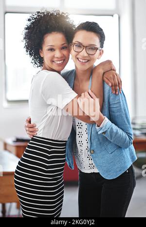 Good coworkers and great friends. Portrait of two female coworkers standing arm in arm in an office. Stock Photo
