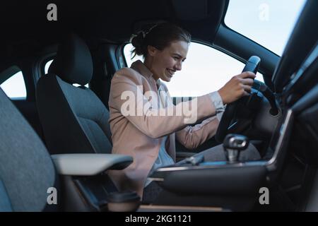 Excited young woman driving her electric car. Stock Photo