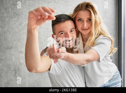 Cheerful man holding wife and smiling while putting apartment keys in her hand. Happy couple wife and husband holding keys from new home celebrating real estate purchase. Stock Photo