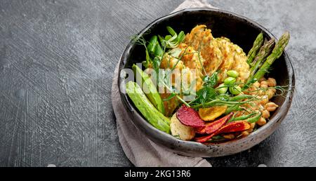 Vegan buddha bowl. Bowl with  vegetables, Zucchini fritters and vegetables chips. Dark background. Healthy eating concept. Top view Stock Photo