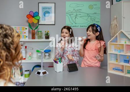 Female students singing using light bulbs as microphones in ecology classroom Stock Photo
