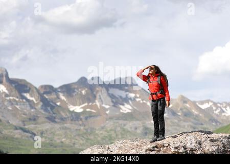 Full body portrait of a hiker in red searching protecting from sun with her hand in the mountain top Stock Photo