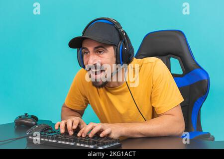 Excited handsome young male gamer playing online game on computer isolated on blue background Stock Photo