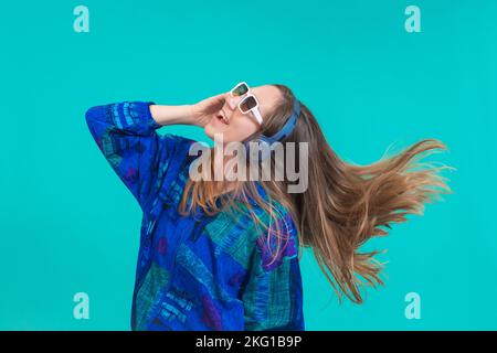 Energy girl with blue headphones listening to music dancing isolated on blue background in studio. Stock Photo