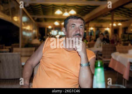 An elderly man of 60 years is sitting at a table in a cafe. A man is waiting for a beer ordered in a cafe Stock Photo