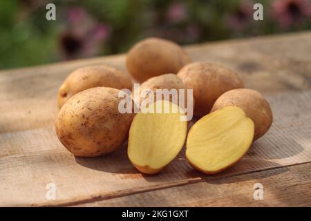 potatoes - a few raw organic potatoes in their skins and one potato cut in half, laid out on a wooden table Stock Photo