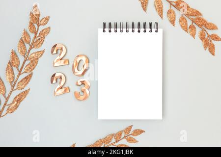 Notepad mock up, glowing decorative branches and 2023 golden numbers on a blue background. New Year wish list concept. Stock Photo