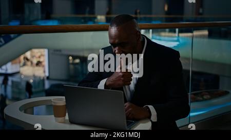Pensive thinking thoughtful African middle-aged adult man worker writer freelancer businessman employer entrepreneur working with laptop in cafe Stock Photo