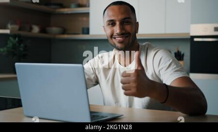 Smiling male winner happy successful African millennial man guy American user freelancer at home kitchen work with laptop satisfied with computer app Stock Photo