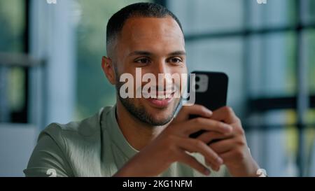 African American businessman browsing smartphone indoors. Multiracial man in office using mobile phone app networking male employer entrepreneur Stock Photo