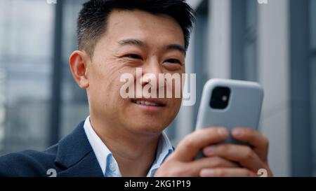 Close up male in city outdoors looking phone screen Asian 40s businessman entrepreneur employer man using mobile app map navigation in smartphone Stock Photo