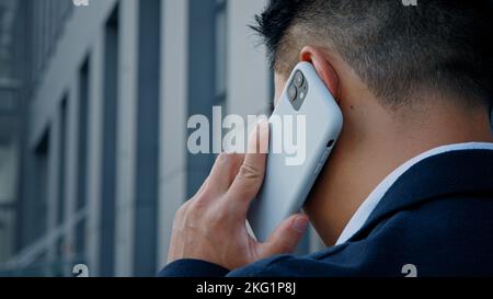 Back view from behind unrecognizable man in formal suit businessman leader salesman talking mobile phone outdoor in city remote distant virtual talk Stock Photo