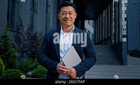 Asian 40s middle-aged businessman entrepreneur employer man worker manager designer financial analyst standing in city near office company building in Stock Photo