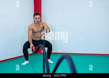 Image of a handsome muscular young man using battle ropes for exercise in a gym. He focuses on performing the exercise. Motivational photo. Copy space Stock Photo