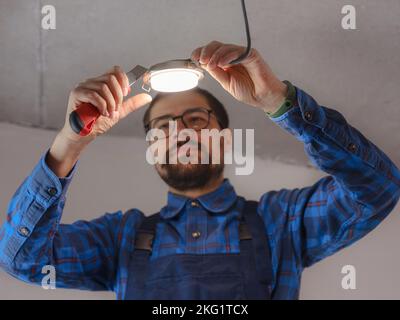 Electrician at work. Service for repair of electrical wiring and replacement of ceiling lamps. builder is installing small lamp on ceiling. Rent-a-gent helps with housework Stock Photo