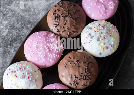 Cupcakes, decorated with icing and sprinkles on a black serving dish. On a dark concrete background Stock Photo