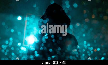 A dark mysterious edit of a hooded figure silhouetted against street lights and bokeh at night. Stock Photo