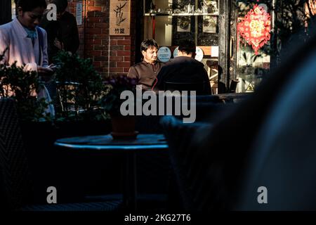 Epsom, Surrey, London UK, November 19 2022, Two Men Sitting Outside A Restaurant Eating And Talking In The Evening Sun With People Passing By Stock Photo
