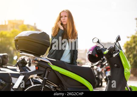 Worried red-haired woman on her motorcycle using smart phone Stock Photo