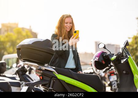 Red-haired woman on her motorcycle using smart phone Stock Photo