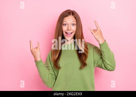 Photo of cheerful positive schoolgirl wear green sweatshirt showing two hard rock gestures isolated pink color background Stock Photo
