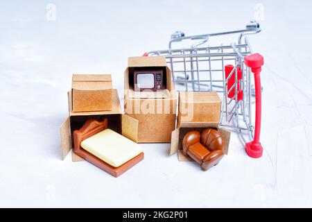 Unpacked tiny delivery boxes with miniature furniture figurines by a small push trolley isolated on white background. Buying furniture for a new apart Stock Photo