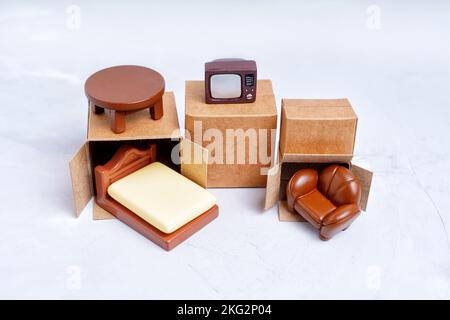 Tiny delivery boxes and miniature furniture figurines isolated on gray background. Moving and furniture shipping concept. Stock Photo