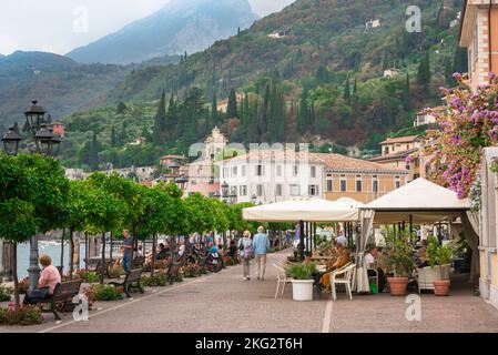 Italian lakes, view in summer of people relaxing beside orange trees lining the lakefront area in the scenic Lake Garda town of Gargnano, Lombardy Stock Photo