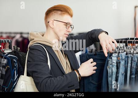 Side view portrait of stylish young man browsing clothes on racks while shopping in thrift store Stock Photo