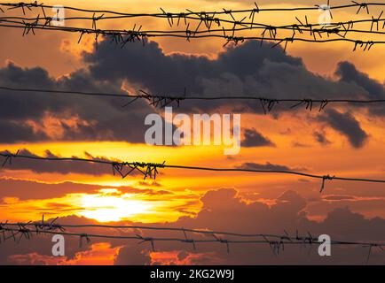 Barbed wire fence in front of Dramatics orange and red sunset or sunrise sky with clouds for background Stock Photo