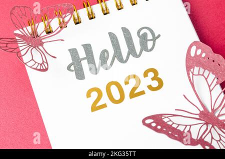 Hello 2023 text on diary and paper butterfly on red background. Stock Photo
