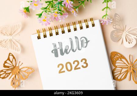 Hello 2023 text on diary and paper butterfly on yellow background. Stock Photo