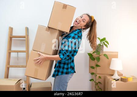 Young woman carrying heavy cardboard boxes in house. Moving to new home concept Stock Photo