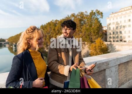 Couple multiracial of friends looking at the mobile phone with shopping bags in hand Stock Photo