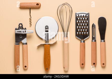 Set of different stainless steel kitchen utensils on beige background top view. Can opener, corkscrew, pizza cutter, whisk, grater, potato peeler and Stock Photo